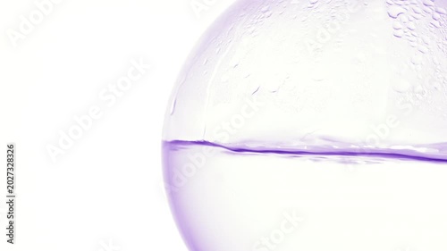 Tight zoom on crystal-like liquid boiling in a round-bottom flask, producing bubbles and condensation on its wall with white background
