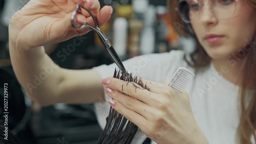Female barber cutting long wet hair of male client with scissors and comb during professional haircut procedure in modern barbershop. Close up shot.