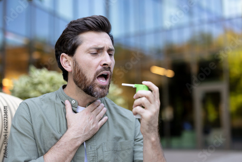 Canvas Print Young man standing outdoors suffering from throat pain, touching his neck, and a