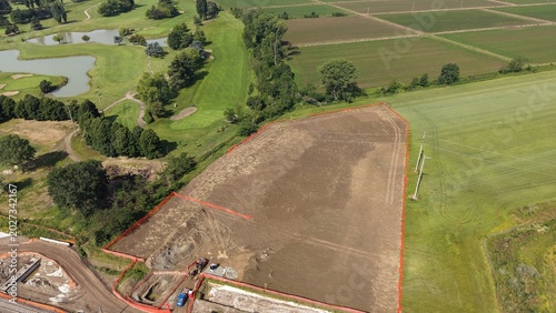 Construction Site in Rural Landscape: An aerial view captures a partially cleared construction site marked with orange fencing, adjacent to a golf course and agricultural fields.