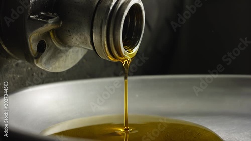 Close-up of motor oil pouring from a motorcycle drain plug into a metal pan, showcasing the fluid's rich amber color and the surrounding mechanical components