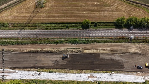 Construction Site Aerial View: An aerial perspective showcases a busy construction site with heavy machinery grading the earth beside a highway, signifying development and progress.
