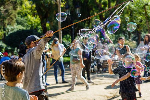 Barcelona, Spain - January 15, 2022. Man in a park making soap bubbles in front of many people and children.