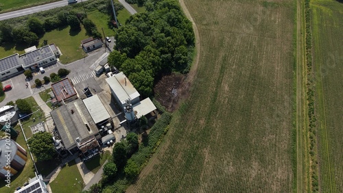 Foto Industrial Park and Farmland from Above: An aerial view showcases a cluster of industrial buildings adjacent to a vast expanse of cultivated farmland