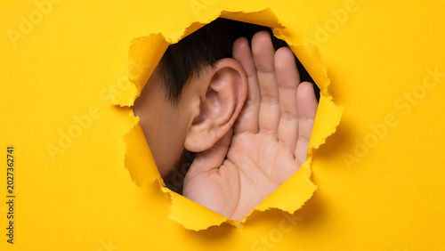 Person's Ear Listening Through a Torn Yellow Paper Hole