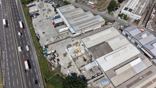 Schilderij op canvas Industrial Zone Next to Highway: An aerial view showcases an industrial zone with warehouses and storage units situated adjacent to a busy highway with moving vehicles