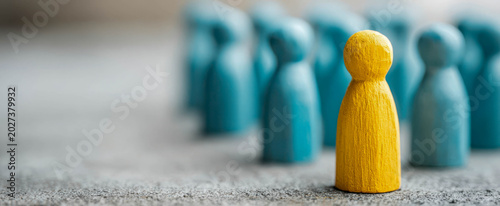 Group of wooden figures with one yellow figure standing out among blue figures in a simple setting