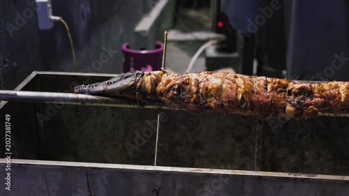 Large whole crocodile roasting on a turning skewer over charcoals for a special meal. This exotic meat is a delicacy in many cultures and is cooked whole for events and parties at night