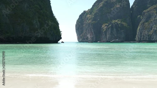 Serene Tropical Beach with Clear Turquoise Water and Towering Cliffs Under Bright Sky Creating Inviting Atmosphere