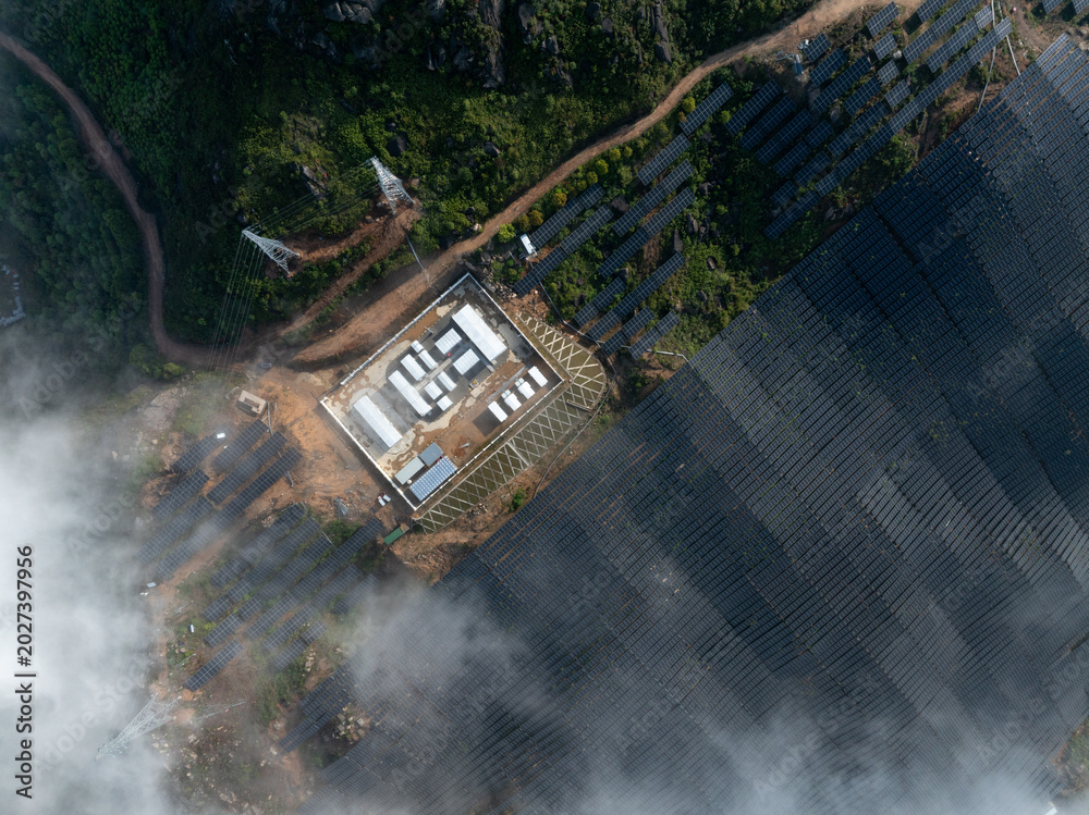 Fototapeta premium Aerial view of mountain solar power station and substation surrounded by clouds and forest