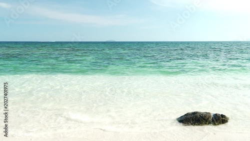 Serene Beach Scene with Clear Turquoise Water, Single Rock on White Sand, and Blue Sky Evoking Tranquility and Gently Lapping Waves