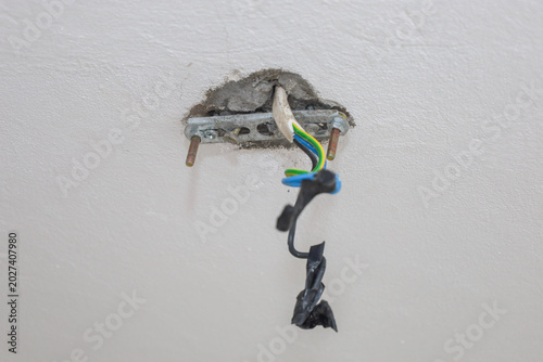 Fotografia Electrical wires and a metal mounting bracket protrude from a hole in the white ceiling during room renovation