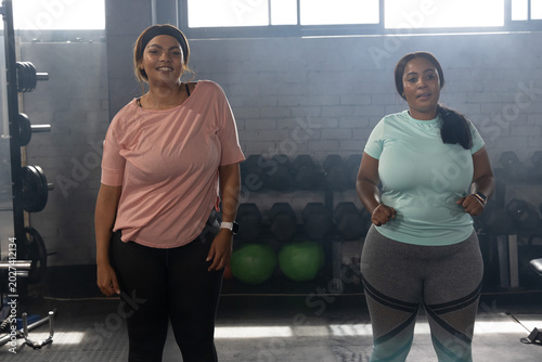 Bild auf Leinwand African American women standing side by side at dumbbell rack in gym wearing ath