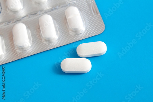 On a blue background lies a blister pack with white oblong tablets.