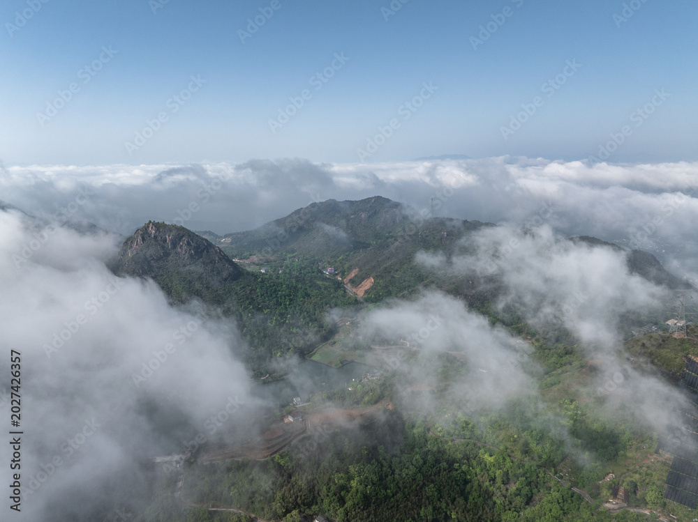 Fototapeta premium Aerial view of lush green mountains surrounded by sea of clouds under blue sky