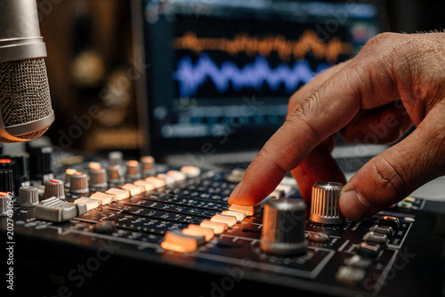 Manos de productor o ingeniero de sonido ajustando los controles de un Ecualizador y faders iluminados de una mesa de mezclas analógica en un estudio de grabación. 