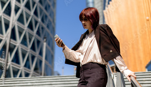 Fotografie Woman checks her mobile phone while walking down stairs in an urban area