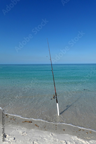 Fotografija Fishing poles stand upright in the sand along a serene beach