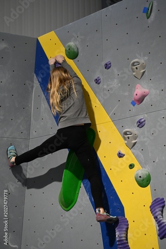 Focused athlete climbing a vibrant indoor bouldering wall, showing strength, balance, and determination in motion at the gym during a tough route run!