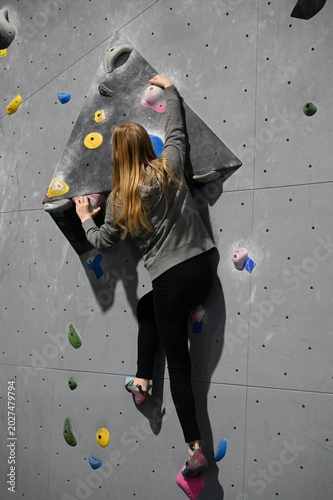 Focused athlete climbing a vibrant indoor bouldering wall, showing strength, balance, and determination in motion at the gym during a tough route run!