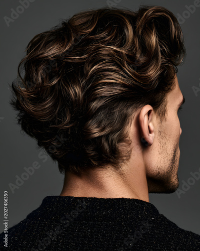 Young man with wavy hair poses against dark background in studio while showcasing hairstyle and hair care techniques during a grooming session
