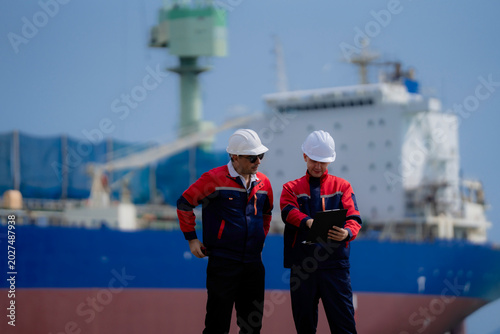 Maritime engineering and cargo logistics concept. Industrial engineers reviewing operational documents and inspection plans at commercial shipping port terminal