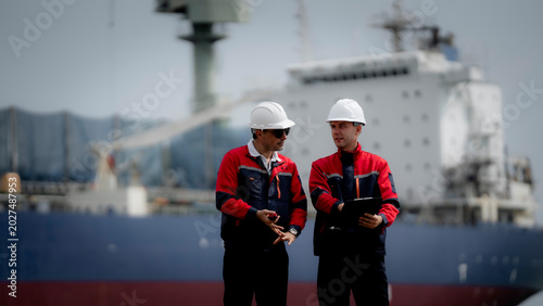 Maritime engineering and cargo logistics concept. Industrial engineers reviewing operational documents and inspection plans at commercial shipping port terminal