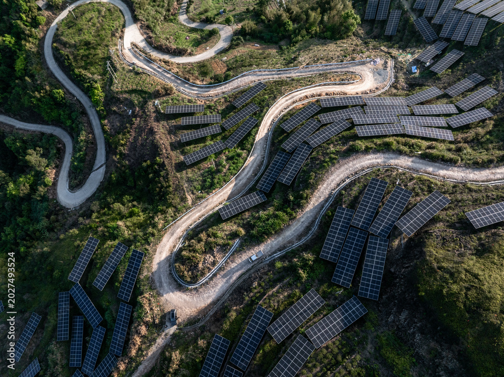 Obraz premium Aerial view of solar photovoltaic power station on mountain terrain with winding roads