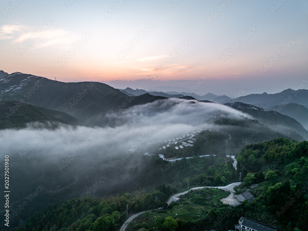 Fototapeta premium Winding mountain road through lush green hills covered in morning clouds and mist