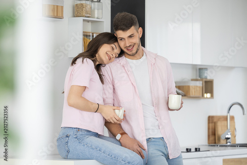 Tableau sur toile Young couple sharing morning coffee in modern kitchen, smiling and affectionate