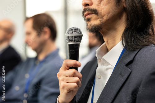 Foto Asian businessman in attendance asking questions during conference panel, engaging in professional debate and listening to speech