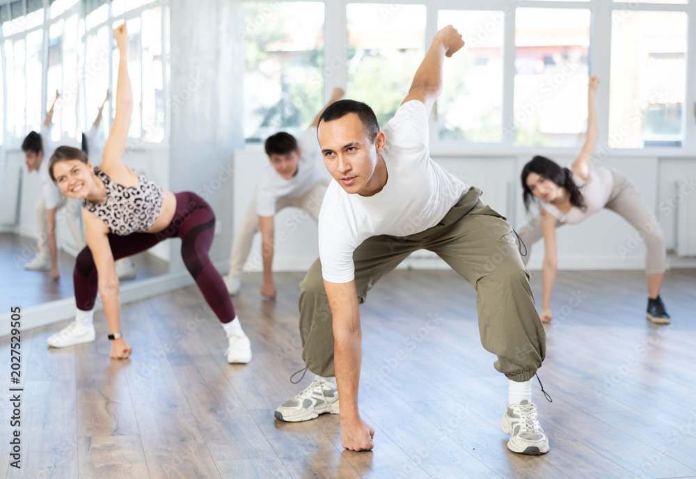 Obraz premium Young guys and girls in sportswear performing hip hop at group dance class