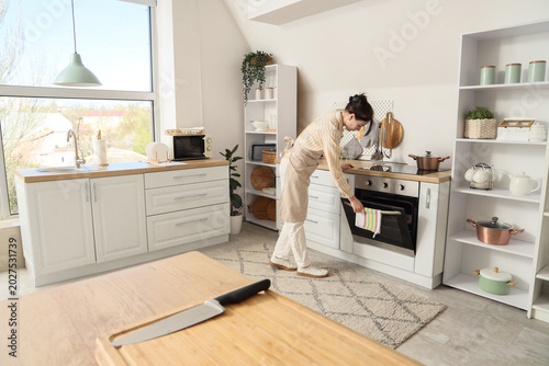 Young woman opening oven in...