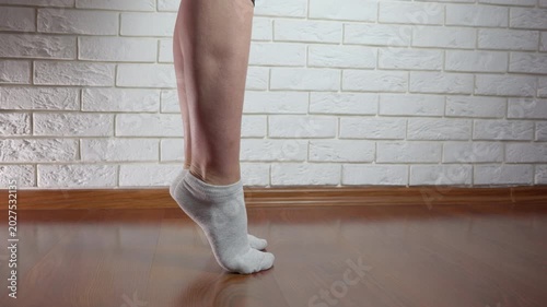 Woman performing calf raises exercise at home. Close-up view of a woman's legs in socks performing calf raises on a wooden floor, strengthening her muscles during a home workout