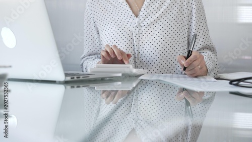 Cuadro en lienzo Unknown businesswoman using a calculator to crunch numbers and jotting down meticulous notes at a sleek glass desk in a contemporary office, closeup view