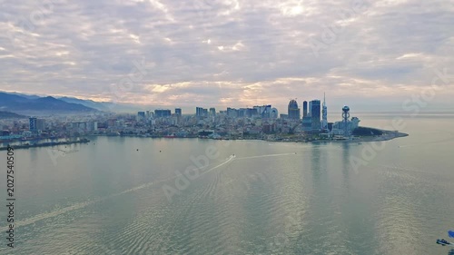 Aerial view of Batumi skyline on the Black Sea coast at sunset. Modern skyscrapers and waterfront reflecting in calm water, scenic cityscape in soft evening light.