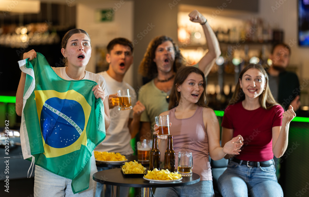 Obraz premium Brazilian fans with the national flag watch the match on TV and express various emotions