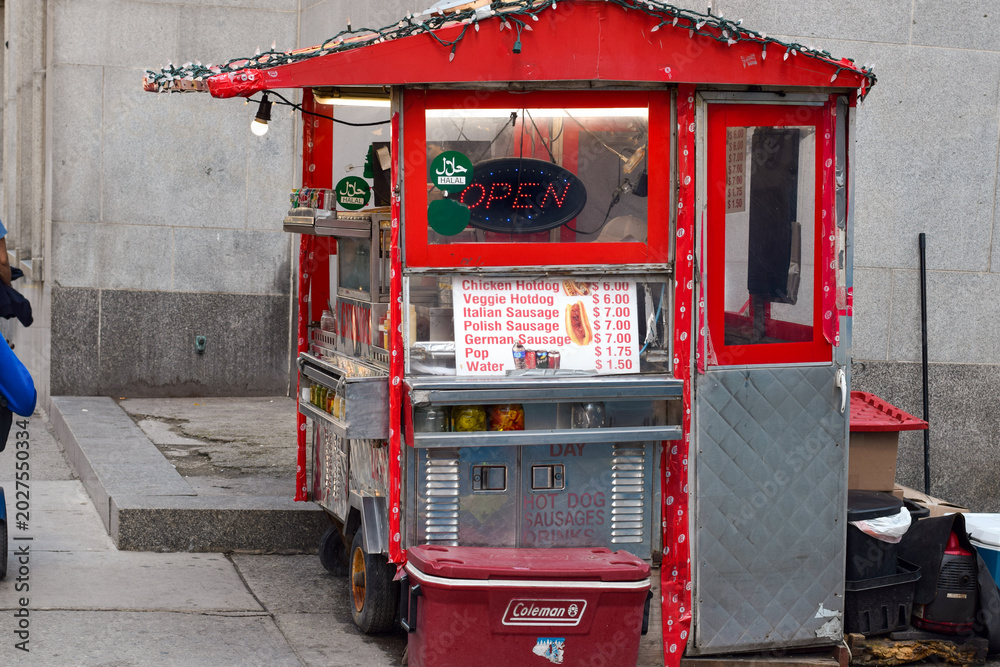 Naklejka premium Red street food hot dog cart on downtown sidewalk with lit up open sign and menu with prices visible, Toronto May 2026