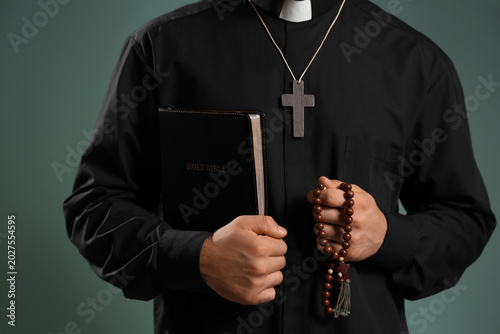 Foto Young priest with wooden cross, Bible and beads on green background, closeup