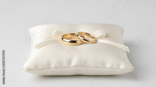 Pair of gold wedding rings on white satin pillow.