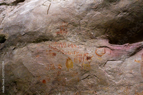 Foto Ancient rock art and pictographs in red and yellow hues, depicting historical imagery on a weathered stone surface
