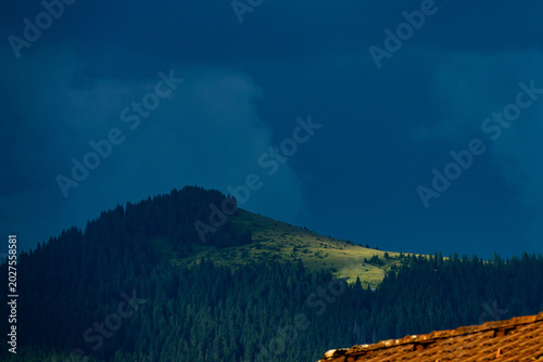 Tableau sur toile A ray of sunshine falls on an alpine pasture on a mountain near Oberstdorf, while the sky is dramatically dark before a rain shower