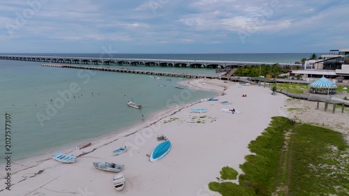 Aerial landscape shot captures a peaceful section of the beach in Progreso, Mexico. The foreground features a sandy path winding through coastal dunes and green scrub vegetation, where several small, 