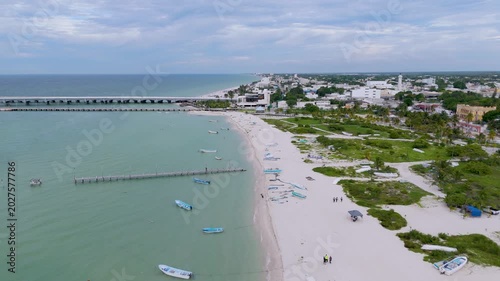 Aerial landscape shot captures a peaceful section of the beach in Progreso, Mexico. The foreground features a sandy path winding through coastal dunes and green scrub vegetation, where several small, 