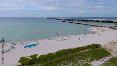Aerial landscape shot captures a peaceful section of the beach in Progreso, Mexico. The foreground features a sandy path winding through coastal dunes and green scrub vegetation, where several small, 