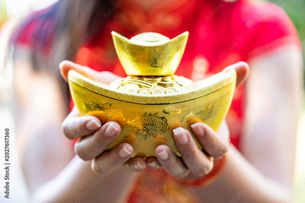 Fototapeta premium The traditional Chinese gold ingot or Sycee, a symbol of wealth and property, in the palms of a lady wearing a traditional Chinese blouse.
