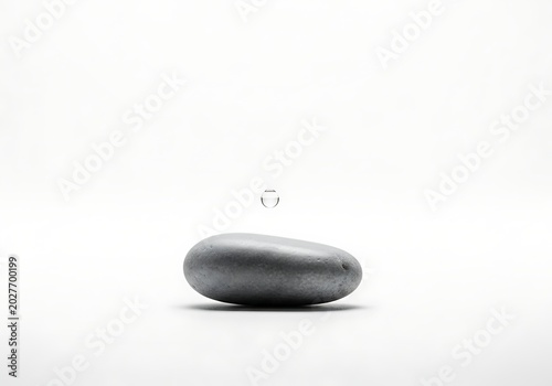 Minimalist composition of a smooth grey stone with a water droplet above