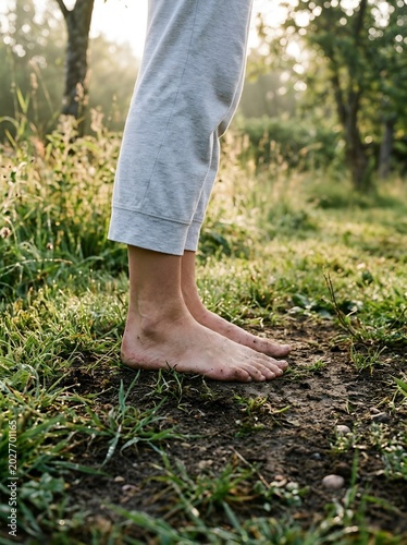 Bare dirty feet standing on moist forest ground at golden hour sunrise, earthing grounding practice in nature with gray sweatpants