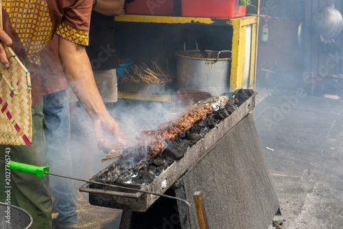 Obraz na plátně A man is grilling Sate Buntel (culinary specialty from Solo, Central Java, Indonesia), featuring minced goat or lamb meat wrap in fat and grilled over charcoal with billowing smoke