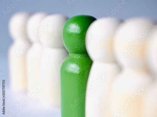 Tableau sur toile Macro shot of a vibrant green wooden peg doll centered between blurred white figures, illustrating the concept of being the center of attention